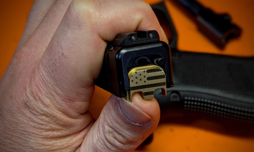 Close-up of a Glock slide showing the backplate being removed with a punch tool